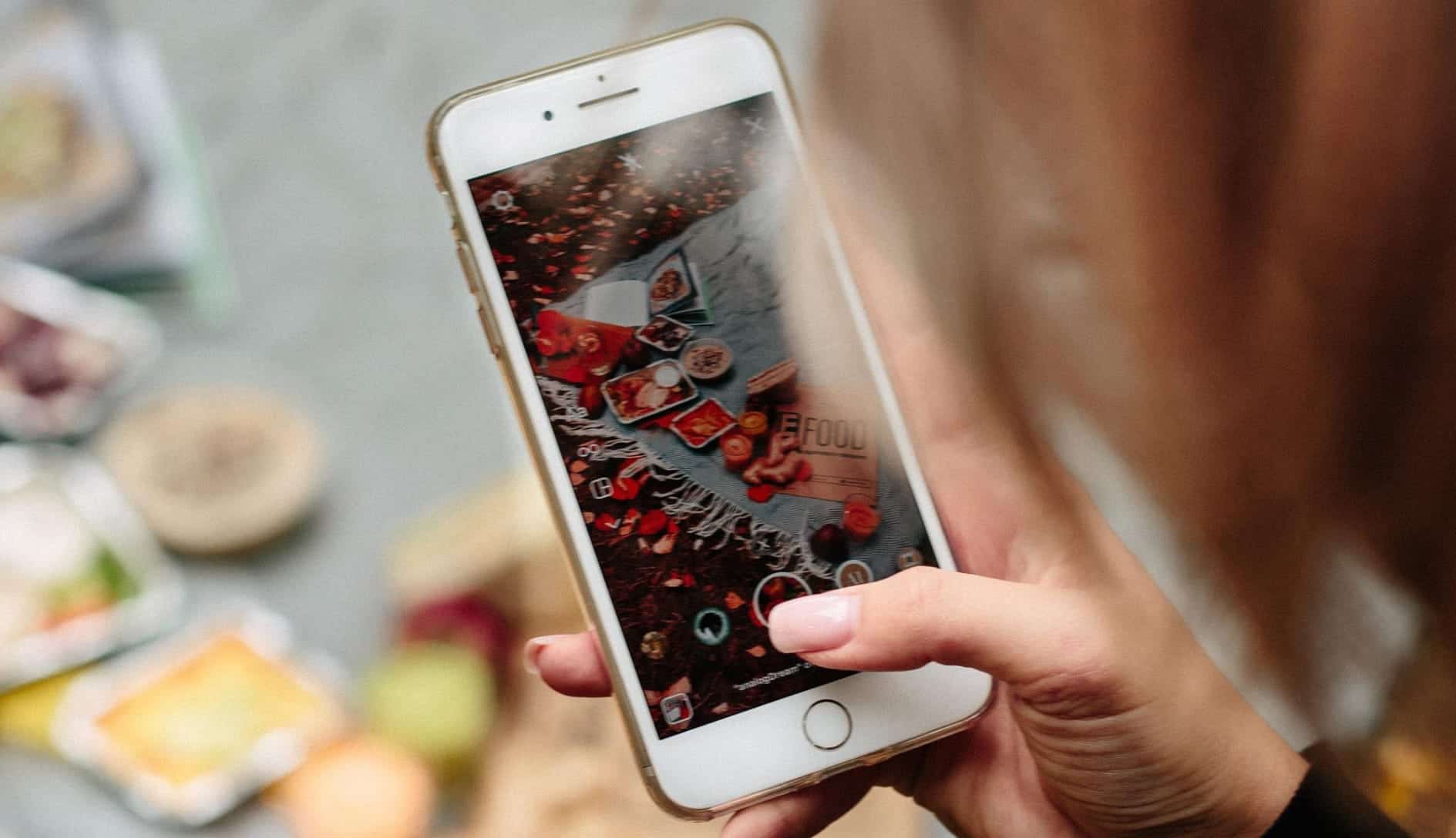 A woman taking a photo of a spread of food using an iPhone
