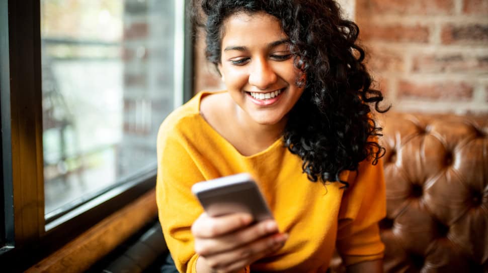 Woman in yellow shirt holding phone and smiling.